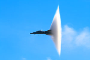 un avion de chasse passe le mur du son et semble traverser un nuage.