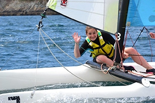 une jeune fille en catamaran en Bretagne salue les animateurs de colonie de vacances